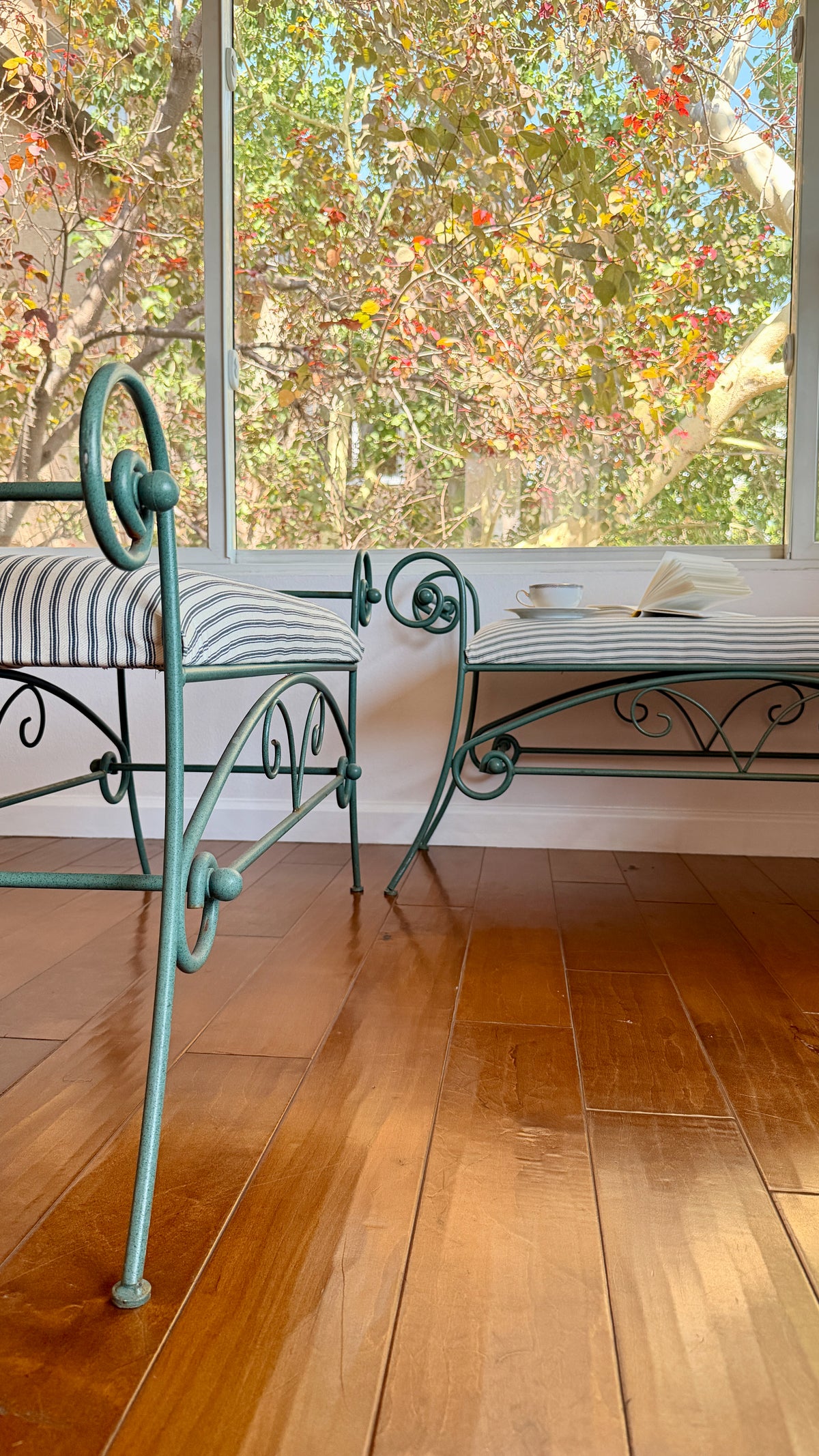 Matched pair of green iron benches shown against a white brick wall