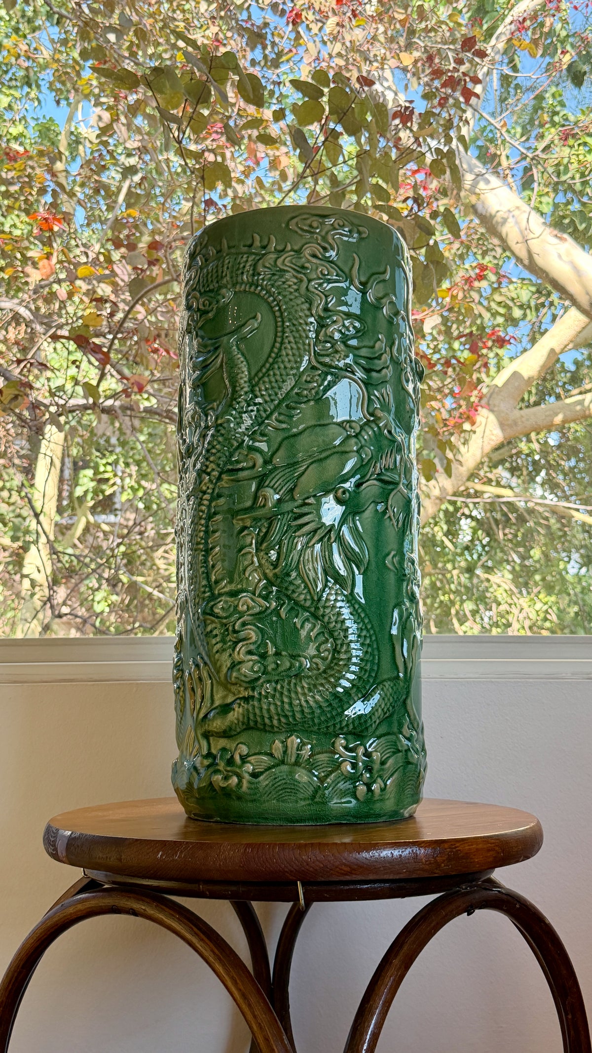 Green crackle glaze umbrella stand with dragons and cloud scrolls in raised relief, shown on a bentwood stand